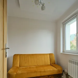 Pokój z musztardową sofą, jasnymi ścianami i oknem